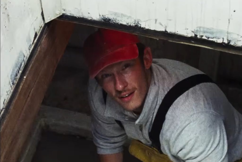 Liam crouches inside the Rose of Nevada's cabin, looking out from beneath a hatch as he explores the mysterious vessel at the centre of the film's time-slip story.