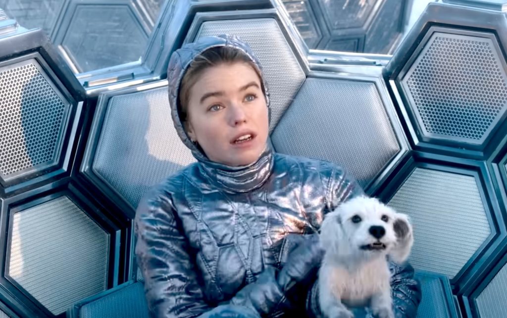 Supergirl, wearing a silver Kryptonian suit, cradles a young Krypto inside a hexagonal Kryptonian spacecraft shortly before escaping Argo City.