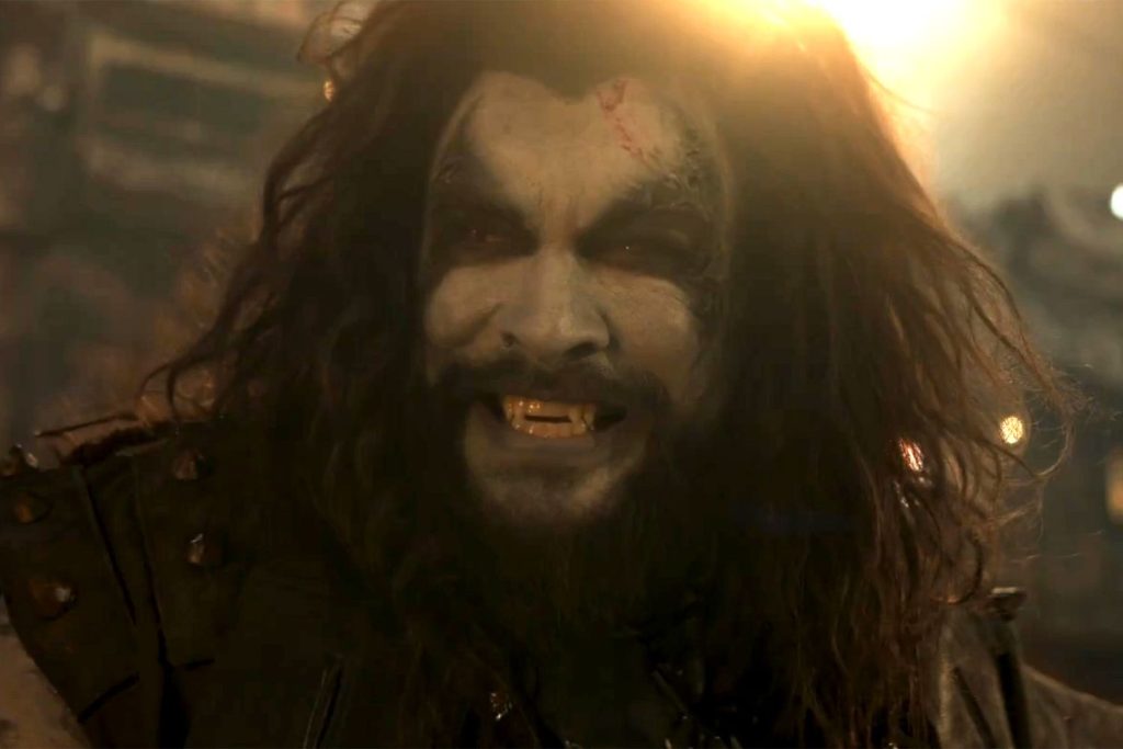Jason Momoa as Lobo grins menacingly in a close-up from Supergirl, showcasing the bounty hunter's comic-accurate appearance.
