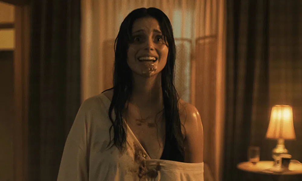 Nikki, drenched and visibly distressed with blood around her mouth, stares ahead in a terrifying moment from Obsession.