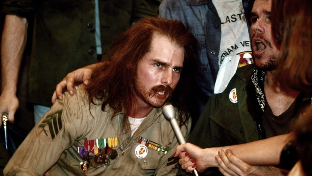 Tom Cruise as Vietnam War veteran Ron Kovic speaks passionately into a microphone while wearing his military medals during a veterans' protest in Born on the Fourth of July (1989).