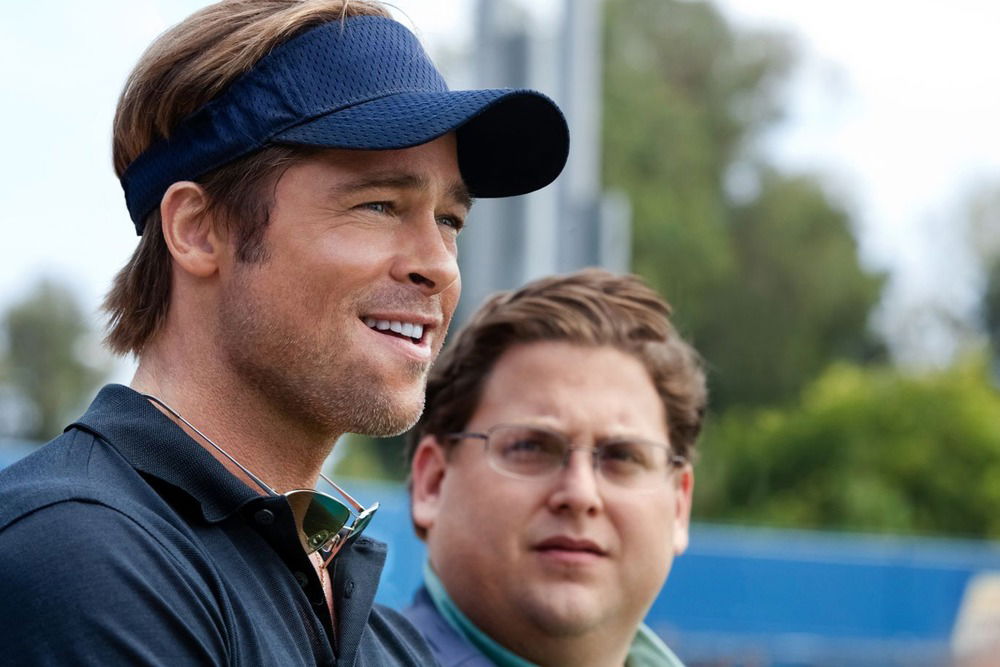 Brad Pitt as Oakland Athletics general manager Billy Beane stands beside Jonah Hill's Peter Brand during a baseball scouting scene in Moneyball (2011).