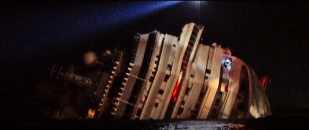 Nighttime view of the Costa Concordia lying capsized on its side, illuminated by rescue spotlights
