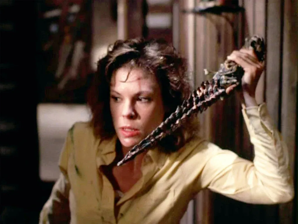 A frightened woman grips the ancient Kandarian Dagger inside a dimly lit cabin, preparing to defend herself against the Deadite threat in Evil Dead II