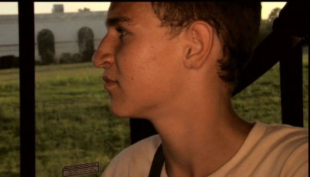 A young man in profile looks out a window in a scene from You Have the Right to Remain Violent (2010)