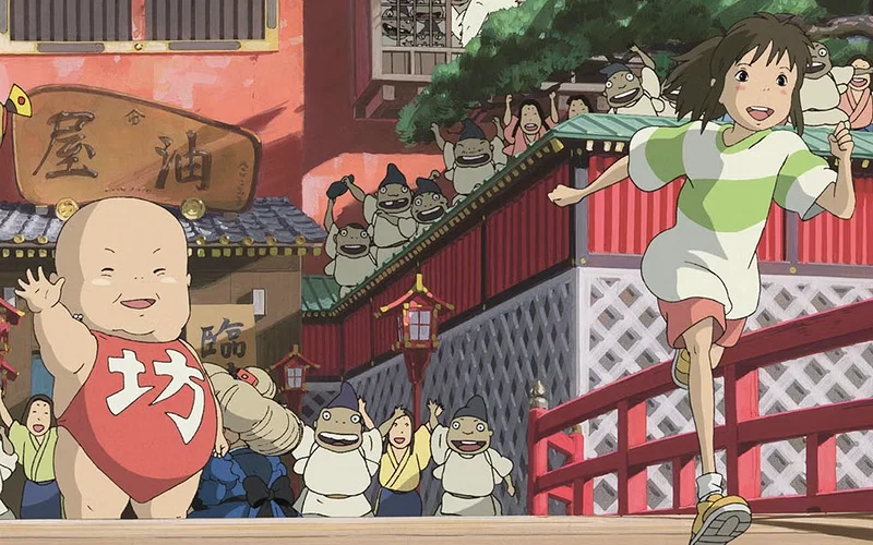 This scene is from the 2001 Academy Award-winning anime film Spirited Away, directed by Hayao Miyazaki. The image depicts the protagonist Chihiro running on a red bridge, chased by spirits from the bathhouse. The giant baby character, Boh, is visible on the left wearing a red bib.
