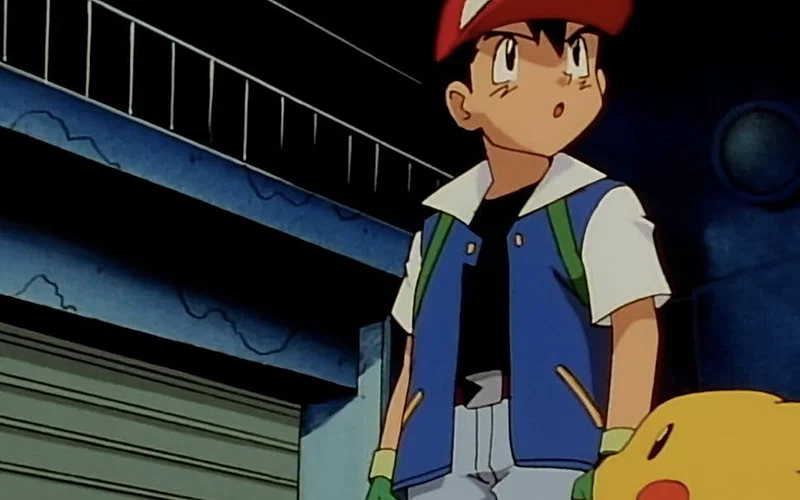 This image features the character Ash Ketchum from the animated series Pokémon: Indigo League. Ash is shown with his signature companion, Pikachu, at the beginning of his training journey.