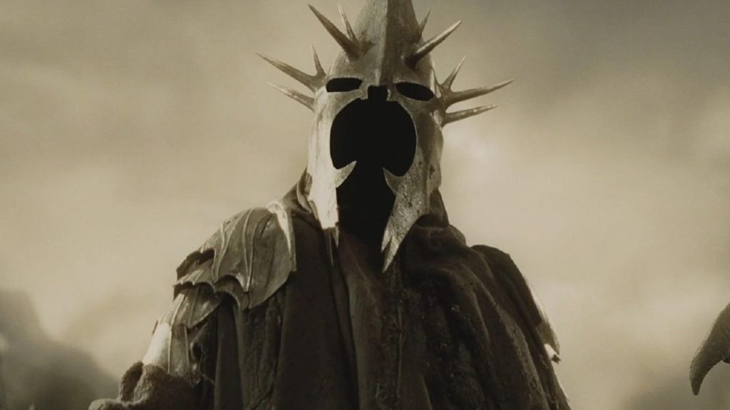 A Ringwraith, clad in dark robes and wearing a spiked crown-like helm, stands motionless on a battlefield in Peter Jackson's The Lord of the Rings film trilogy.