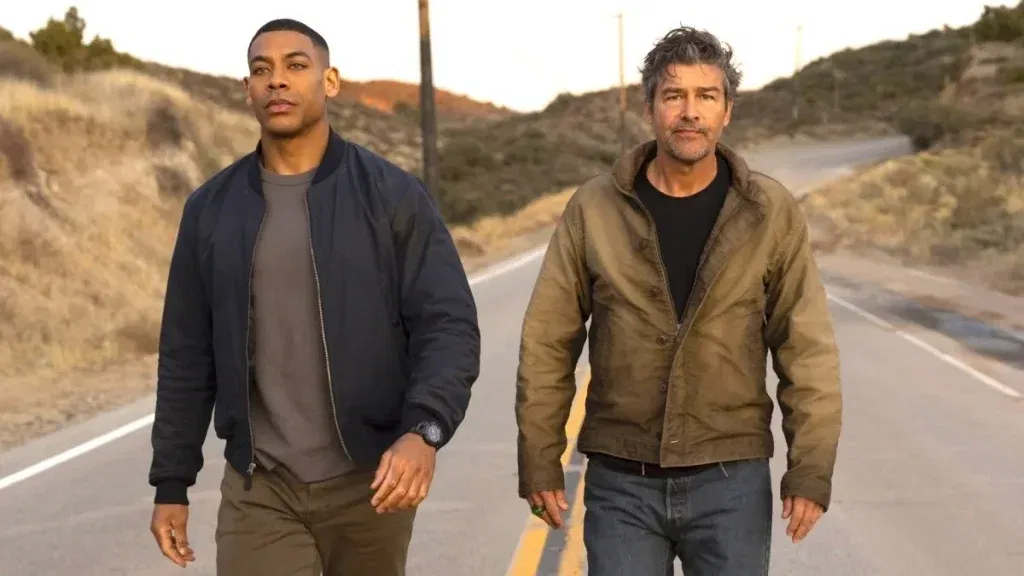 Aaron Pierre as John Stewart and Kyle Chandler as Hal Jordan walking together down a rural two-lane road at dusk in a promotional image for HBO's Lanterns.