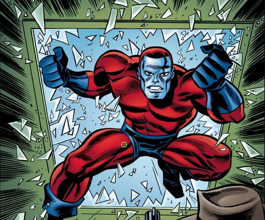 Comic book illustration of a Manhunter — a blue-skinned android with a red-and-blue uniform and a target-crosshair emblem on its thigh — bursting through a shattered green-framed window with fists raised.