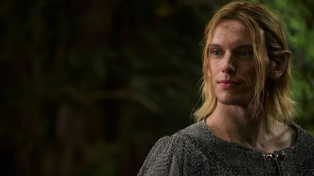  The Rings of Power Season 3, wearing chainmail armor with a forest backdrop, looking off to the side with a pensive expression.