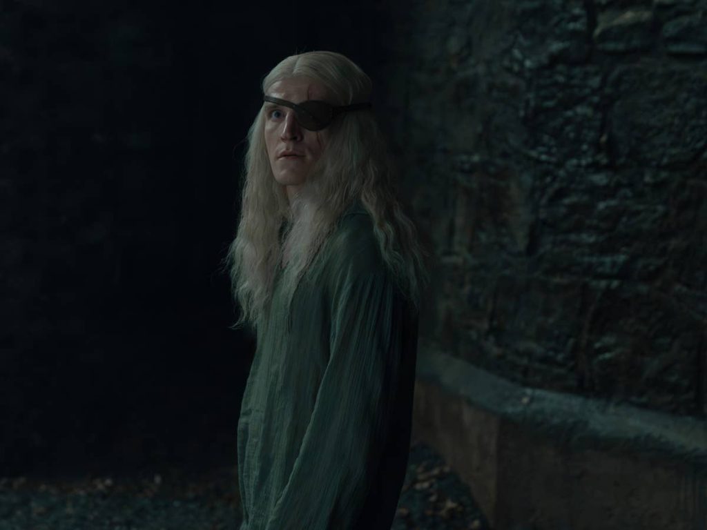 Aemond Targaryen, wearing an eyepatch, stands inside Harrenhal in House of the Dragon.