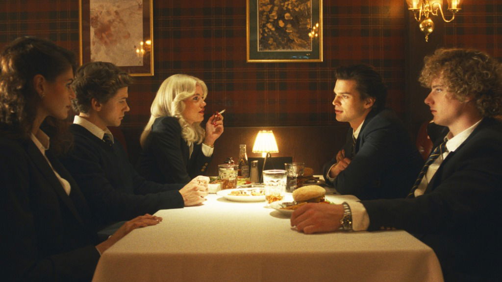 Five young adults in school uniforms in The Shards sit across from each other at a restaurant table during a tense dinner scene in The Shards.