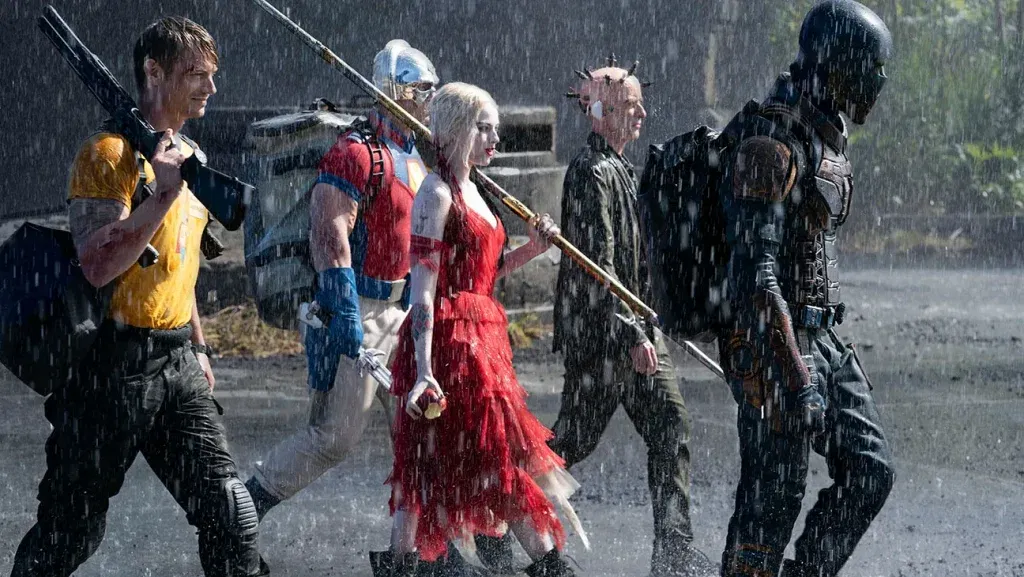 Members of Task Force X walk through heavy rain carrying weapons in a scene from The Suicide Squad (2021).