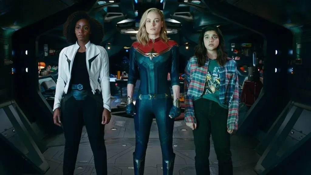 Three superheroes stand side by side aboard a spacecraft, with Captain Marvel in the center flanked by Monica Rambeau and Ms. Marvel in The Marvels.