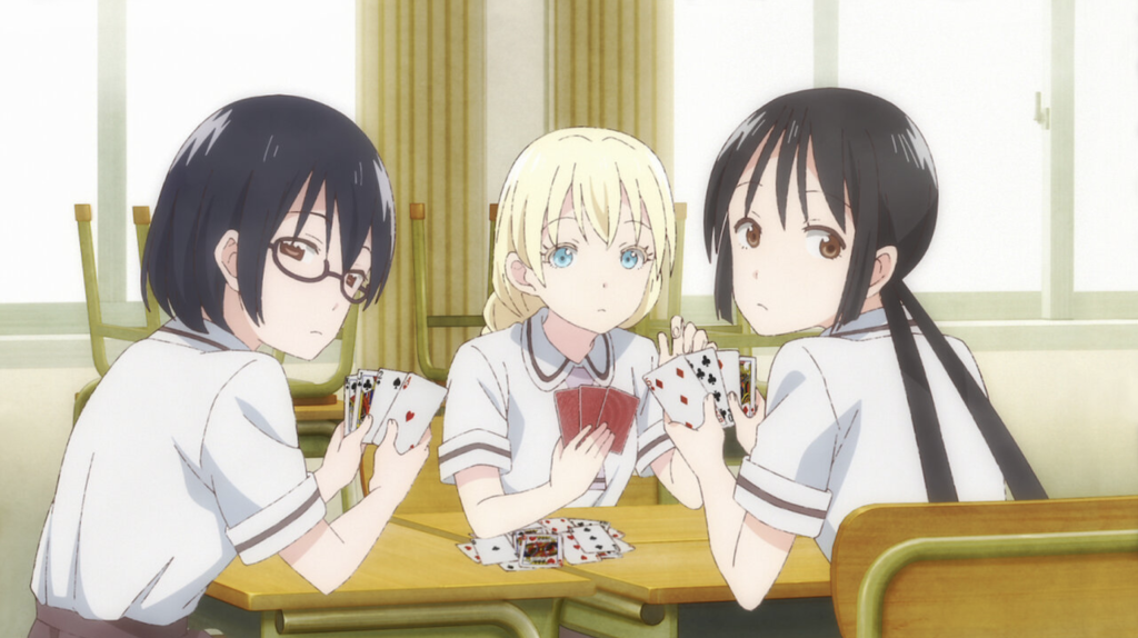 The Most Underrated Comedy Anime of Each Year From the 2010s, Ranked 12 The image features the main trio—Kasumi Nomura, Olivia, and Hanako Honda—playing cards together in the comedy anime series Asobi Asobase: Workshop of Fun. Kasumi Nomura (wearing glasses), Olivia (the blonde transfer student), and Hanako Honda (with her hair tied in long twin-tails).