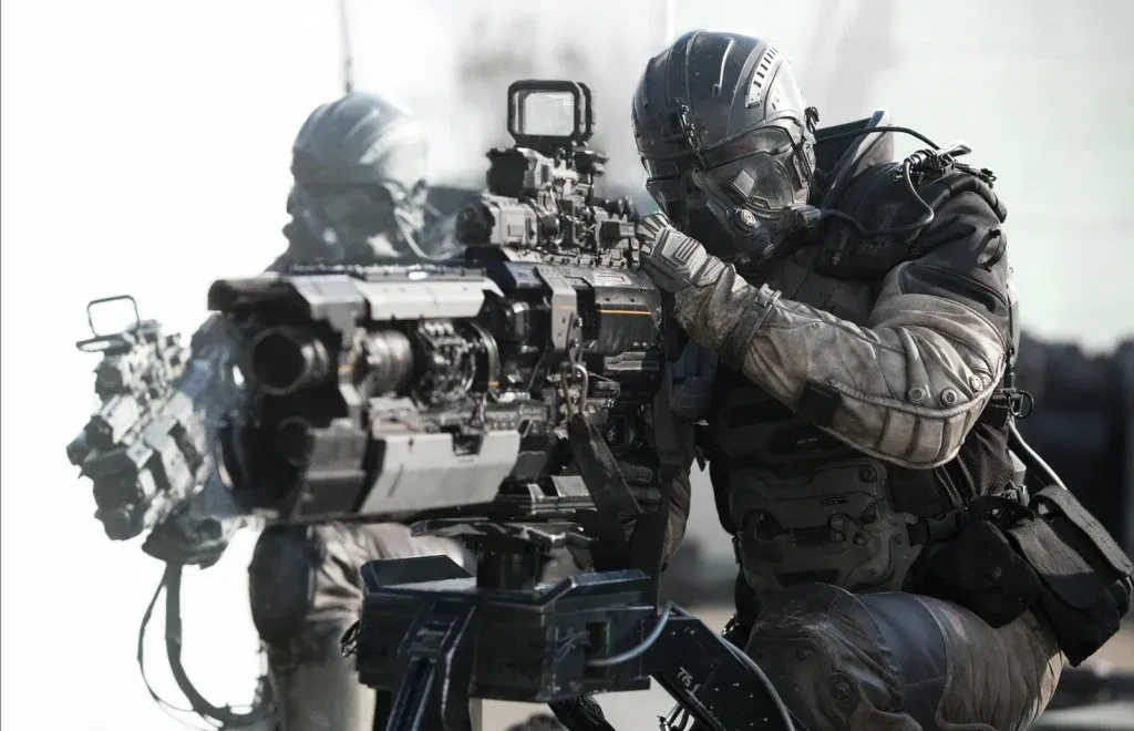 Two soldiers in full tactical exosuits and visored helmets crouch behind a mounted heavy weapon fitted with advanced targeting optics.