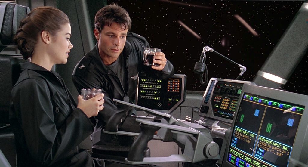 Two officers in dark flight jackets sit at a starship's illuminated control console, holding drinks as they talk, with a starfield visible through the viewport behind them.