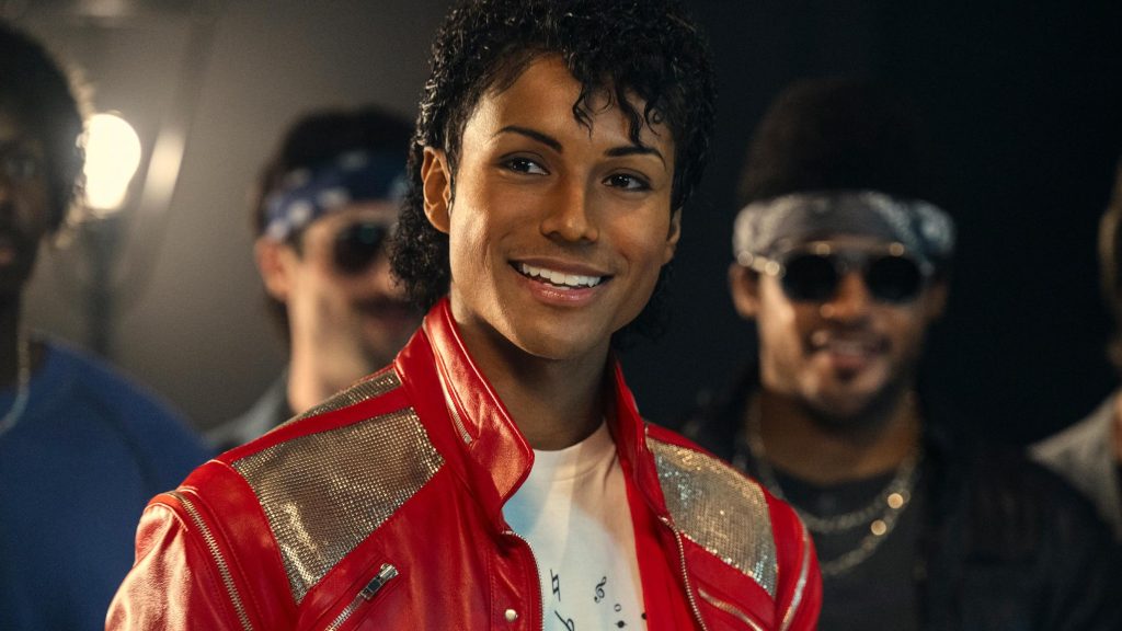 Jaafar Jackson as Michael Jackson smiles in a red and silver leather jacket in a still from Michael