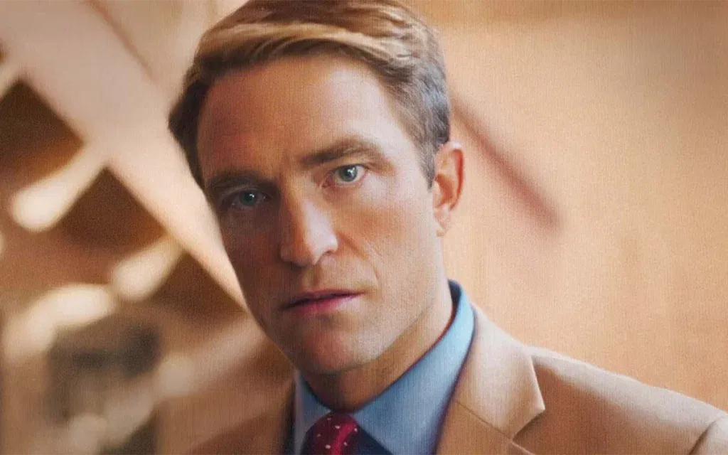 Robert Pattinson in a beige suit and red tie.