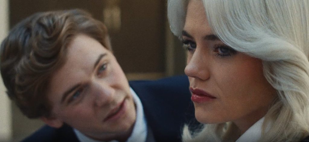 The Shards Episode 6 And 7 Ending Explained: Why Did Rhonda Accuse Susan Of Kidnapping Her? 4 A young man in a navy suit leans in close to a woman with platinum-blonde hair and dark red lipstick, the two locked in a charged, quiet exchange in The Shards.