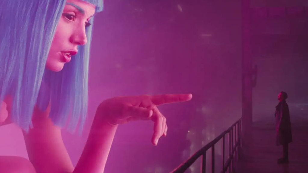 Joi's giant hologram gestures toward K on the balcony in Blade Runner 2049