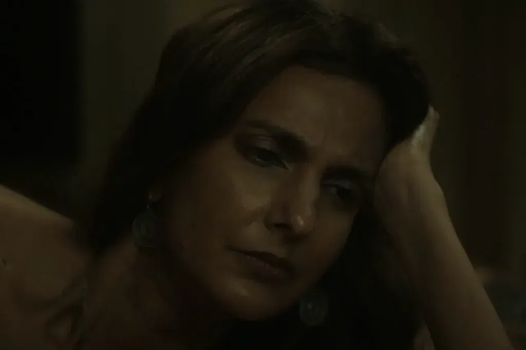 Zoe (Poorna Jagannathan) in a dimly lit close-up, her expression troubled as she rests her head against her hand, in a quiet moment from Lanterns episode 4.
