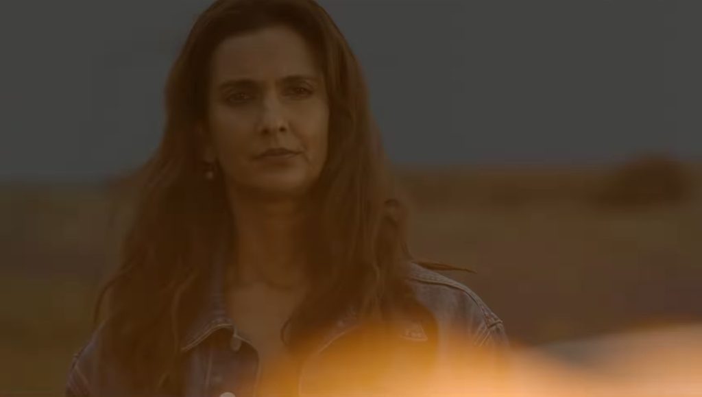 Zoe Macon stands with the scene lit by an explosion, her expression mysterious