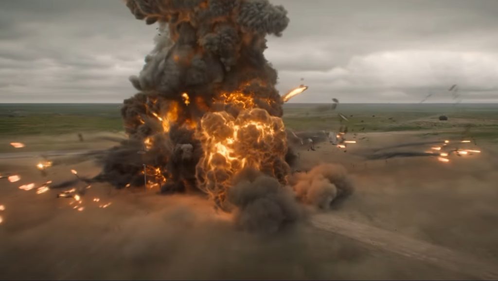 A massive fireball and plume of black smoke erupt over an open field outside Rushville, with debris scattering across the surrounding road and grassland.
