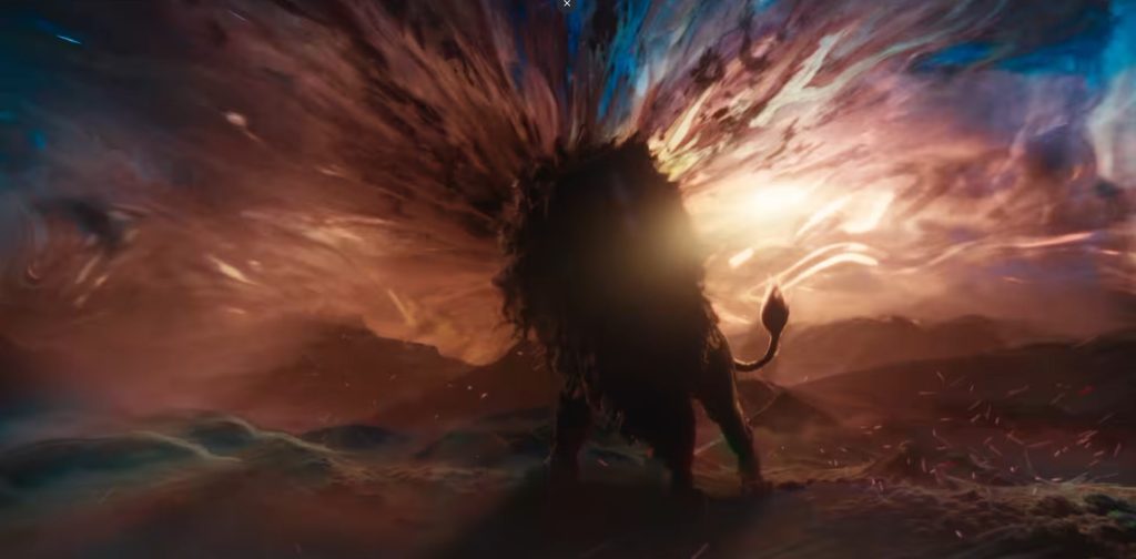 Silhouette of Aslan, his mane blown outward into streaks of orange, red, and blue light, standing on a rocky landscape with a glowing burst behind his head. He is singing narnia into existence