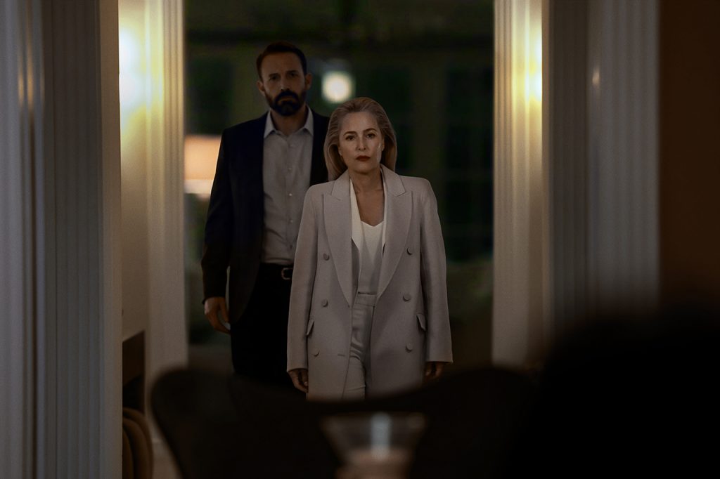 a woman in a light suit and a man in a dark suit stand in a dimly lit hallway, framed by white columns, facing the camera with serious expressions, suggesting a tense or formal setting. Ben affleck in animals